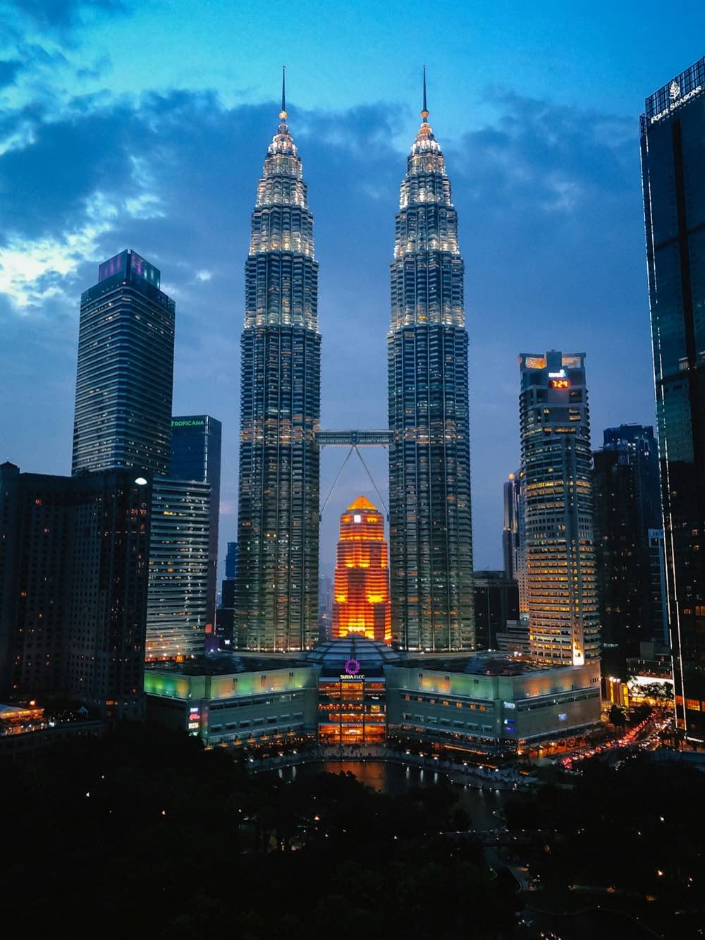 Kuala Lumpur skyline at blue hour, the Petronas Towers lit against a clouded sky
