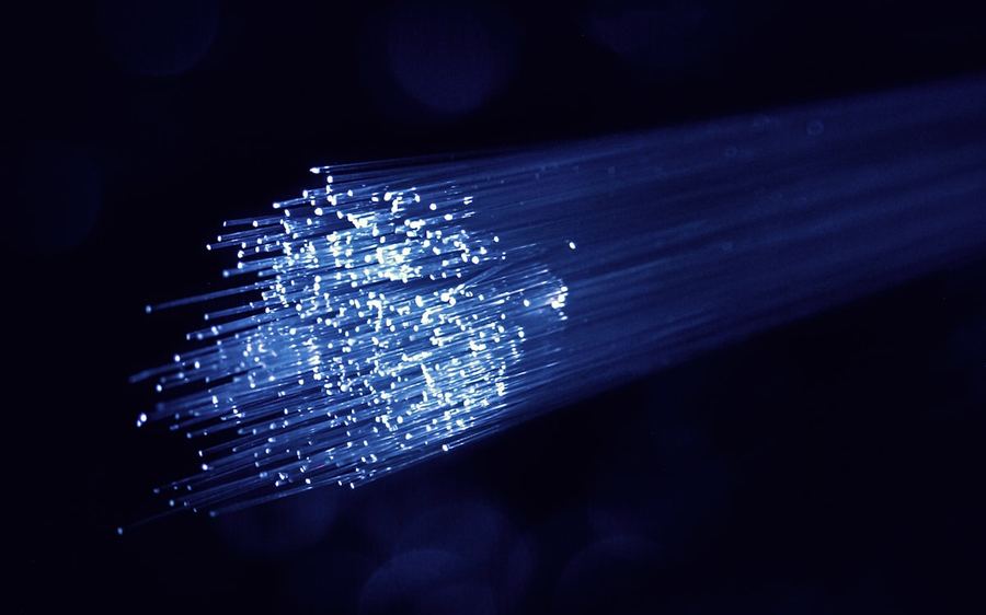 A bundle of optical fibres carrying blue light through darkness