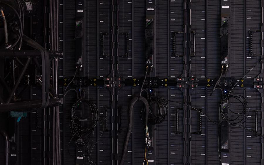 A dark aisle of server racks with patch cables running between them